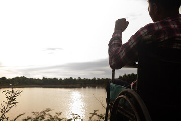 Young disabled man with river background.He is sitting on wheelchair and looking into river.despair,lonely,hope.Photo concept depression and Patient.