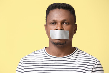Sad African-American man with taped mouth on color background. Stop racism
