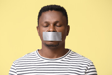 Sad African-American man with taped mouth on color background. Stop racism