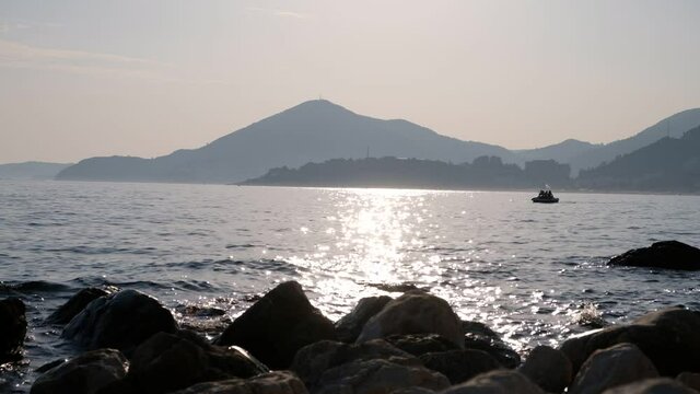 Seashore at sunset with rocks in the foreground and mountains in the background. The sun's rays are reflected in the water. Beach of Kamenovo in Montenegro at sunset