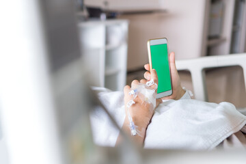 Health care technology concept, Blank Green Screen Mock up smartphone for Text, Hospital Patients woman senior using smart phone while Recovering moment whith saline, Iv drip, intravenous needle