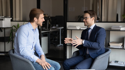 Happy young caucasian businessmen sit in office talk joke and laugh in office during work break,...