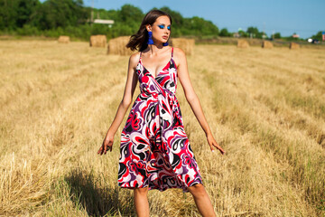 Portrait of a young woman with bright makeup posing on a mown wheat field