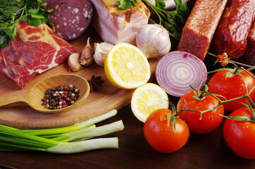 Sausage, ham and meat products, spices, tomatoes, herbs on the kitchen board.
