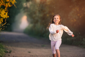 girl junior schoolgirl runs along the road in the evening in the park, happy face, bright emotions,...