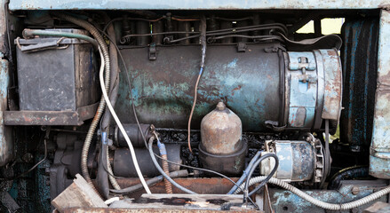 Close-up on an old rusty tractor or truck engine with a battery and oil drips during repair in a workshop. Auto service industry.