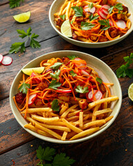 Loaded French Vegan Fries with tofu, pickled vegetables radish, carrot and spicy hot sauce on rustic wooden table