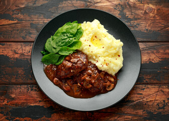Salisbury Steak with mushroom gravy, mashed potatoes and spinach on rustic wooden table
