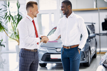 Fototapeta premium confident caucasian dealer or salesman shaking hands to customer in dealership. man going to make purchase
