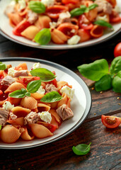 Conchiglie Tuna pasta with tomato sauce, feta cheese and basil on wooden table. healthy food