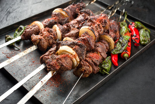 Traditional Russian lamb shashlik on a barbecue skewer with chili, onion and sumach as close-up on a rustic metal tray