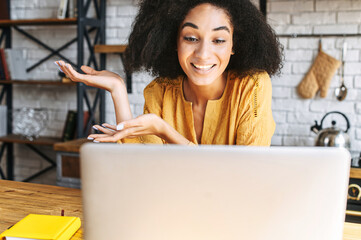 Distance communication with friends via video call. A young attractive black woman talking via video with her friend, she looks at webcam with a cheerful smile. Close-up front view