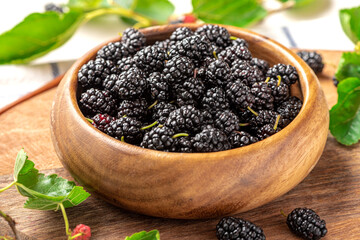 Fresh black mulberry in a wooden bowl and leaves on the table. Mulberry close-up.