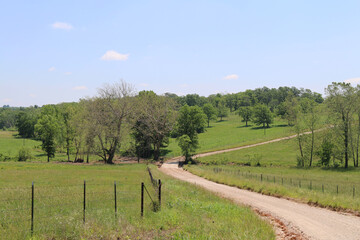 a curving country fence lined dirt road winding through a lush rural hilltop perfect for seasonal marketing as well as cards posters signs and background backdrop wallpaper © DrewDuzz