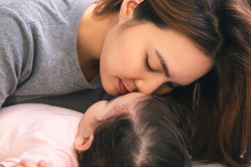 Close up young mother kissing her baby or infant girl while adorable toddler daughter sleeping on bed with love. Beautiful single mother love and care baby so much. Asian mother give big kiss
