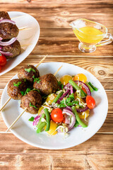 Lula kebab from lamb on a wooden skewer with a salad from Cherry tomatoes, red onions and green beans. A white plate on an old wooden background. Selective focus.