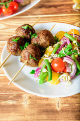 Lula kebab from lamb on a wooden skewer with a salad from Cherry tomatoes, red onions and green beans. A white plate on an old wooden background. Selective focus.