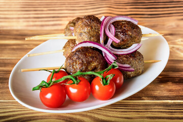 Lula kebab from lamb on a wooden skewer with a salad from Cherry tomatoes, red onions and green beans. A white plate on an old wooden background. Selective focus.