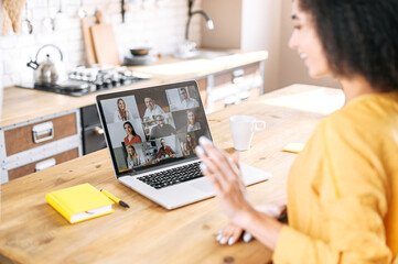 Virtual conference, webinar. A young mixed-race woman waves hello to many diverse people on the laptop screen
