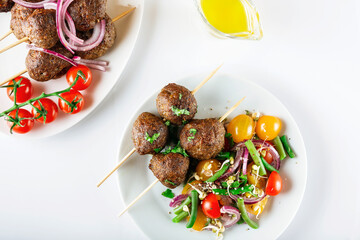 Lula kebab from lamb on a wooden skewer with a salad from Cherry tomatoes, red onions and green beans. White background. Selective focus.