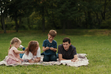 Fototapeta premium Happy young couple spending time with their daughter and son outdoors in the nature. Weekend activities concept