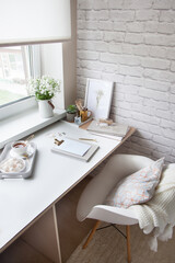 Work table near the window in the Scandinavian Nordic style. Female work and home office concept. White and gold office. Flowers in a vase and rings, bracelets on the table.