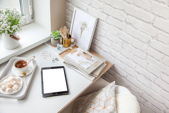 Work Table Near The Window In The Scandinavian Nordic Style. Female Work And Home Office Concept. White And Gold Office. Flowers In A Vase And Rings, Bracelets On The Table.