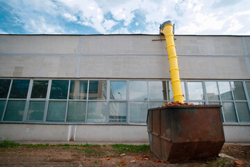Yellow garbage chute loaded dumpster in front of old factory under construction. Loaded dumpster...