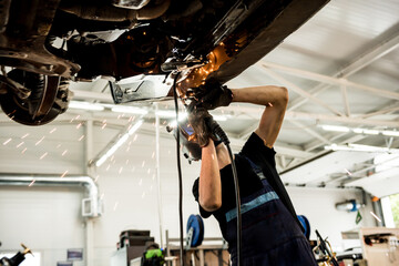 Car mechanic with protective mask welding car. Service station