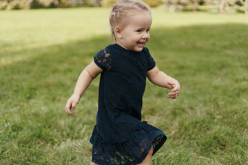 Little cheerful blonde girl wearing a navy dress running in the grass, enjoying life