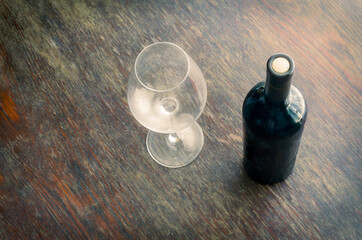 Sealed bottle of red wine and an empty wine glass on the wooden table.