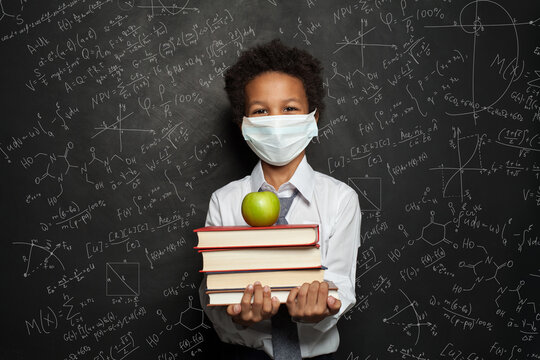 Happy Child In Medical Protective Face Mask Holding Books And Green Apple On Blackboard Background