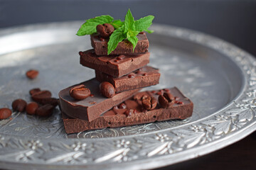 Pieces of dark chocolate and a sprig of mint on a silver tray.