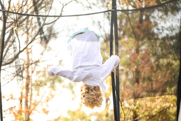 Young caucasion boy doing flip on trampoline. Upside down trick in air.