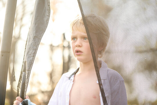 Young boy standing on trampoline with white shirt unbuttoned