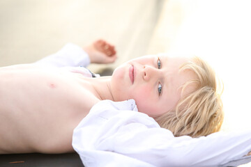Obraz na płótnie Canvas Blonde hair blue eyed boy lying on trampoline with white shirt undone