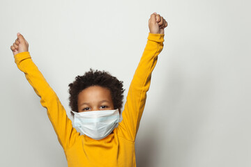 Portrait of happy black child boy in medical protective face mask holding hands up