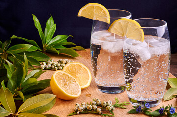 Two glasses of lemonade on wood surrounded by green leaves and 2 half lemons.