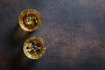 Twoshot of whiskey with ice cube on dark brown background. View from above. Copy space.