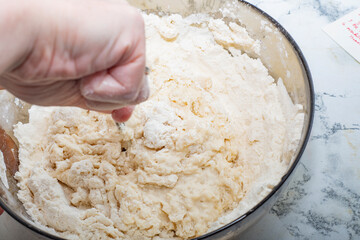 Thick dough is manually mixed in a transparent bowl.