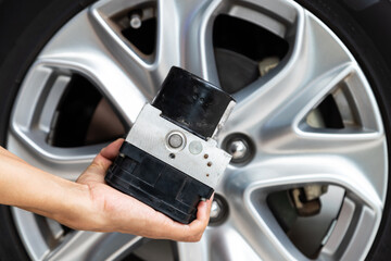 Hand holding ABS modulator of the brake system with a magnetic valve for car with wheel in back.