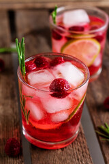 Cold  fresh summer berry lemonade with rosemary,raspberry and ice in glass on wood background