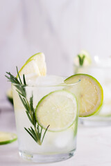 Cold  fresh summer cocktail with lime, mint,rosemary and ice in glasses on a light background