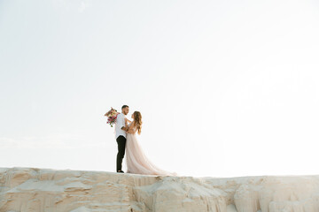 Love Story of a beautiful couple in a pink wedding luxury dress with a bouquet in the Sahara...