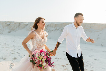 Love Story of a beautiful couple in a pink wedding luxury dress with a bouquet in the Sahara...
