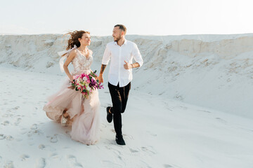 Love Story of a beautiful couple in a pink wedding luxury dress with a bouquet in the Sahara...
