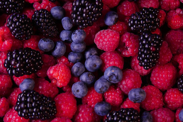 Fresh berries composition. Raspberries, blackberries and blueberries on black background. Tasty looking organic fruits covered with dew.