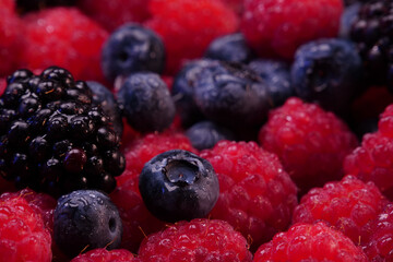 Fresh berries composition. Raspberries, blackberries and blueberries on black background. Tasty looking organic fruits covered with dew.