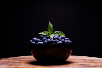 Blueberries with dew and leaves of mint on wooden desk and black background. Summer background, bowl full of raw food for vegan. Fresh and tasty forest berries wallpaper