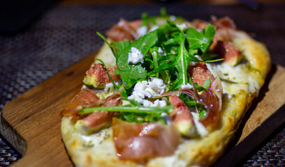 Selective focus. Pizza with prosciutto (parma ham), arugula (salad rocket) and parmesan on dark wooden background. Prosciutto di Parma sandwich with figs and mozzarella cheese.